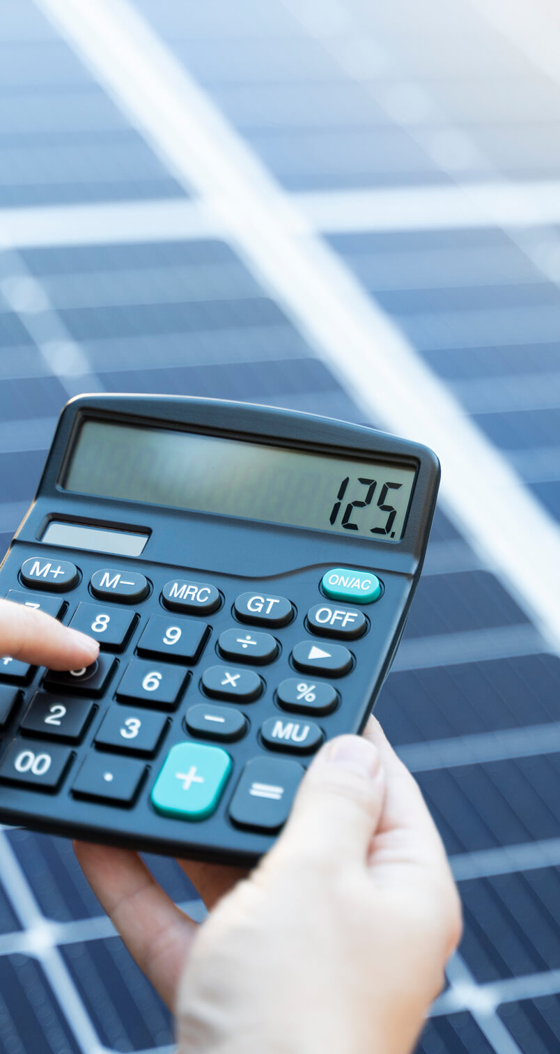 A person uses a calculator displaying 125 in front of solar panels.