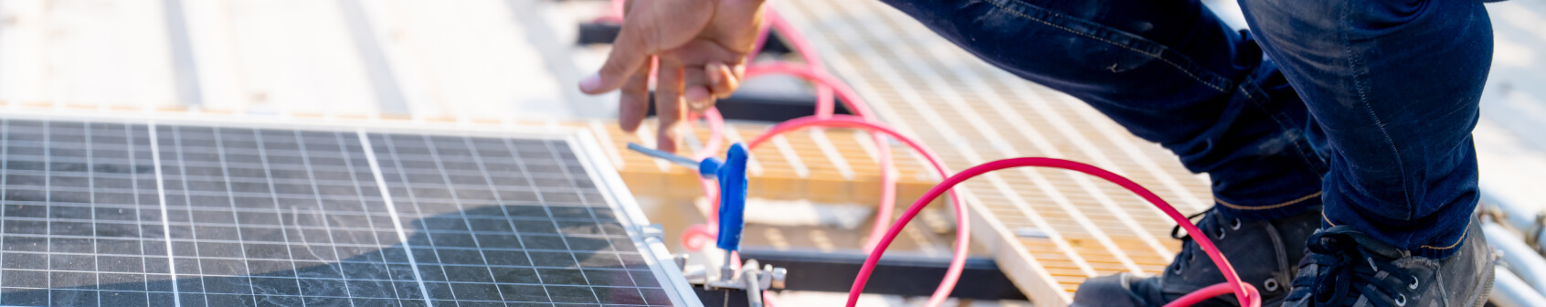 Wearing jeans and boots, a person works on solar panel installation with tools and red electrical wires on a rooftop.