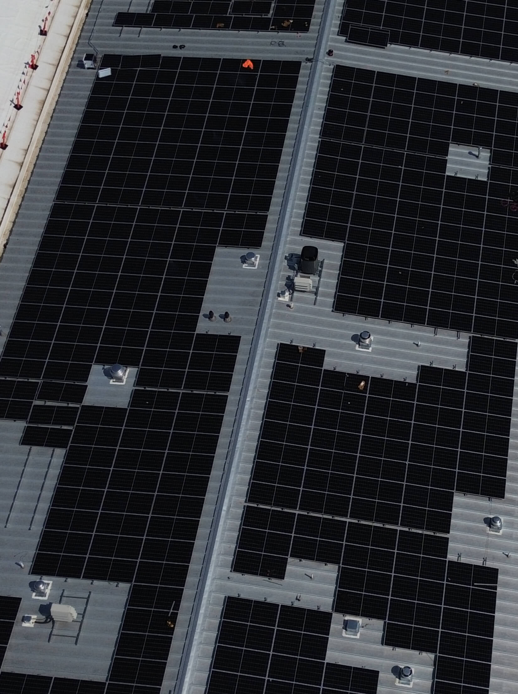 Aerial view of a large rooftop covered with solar panels, their sleek black surfaces intersected by metal walkways.
