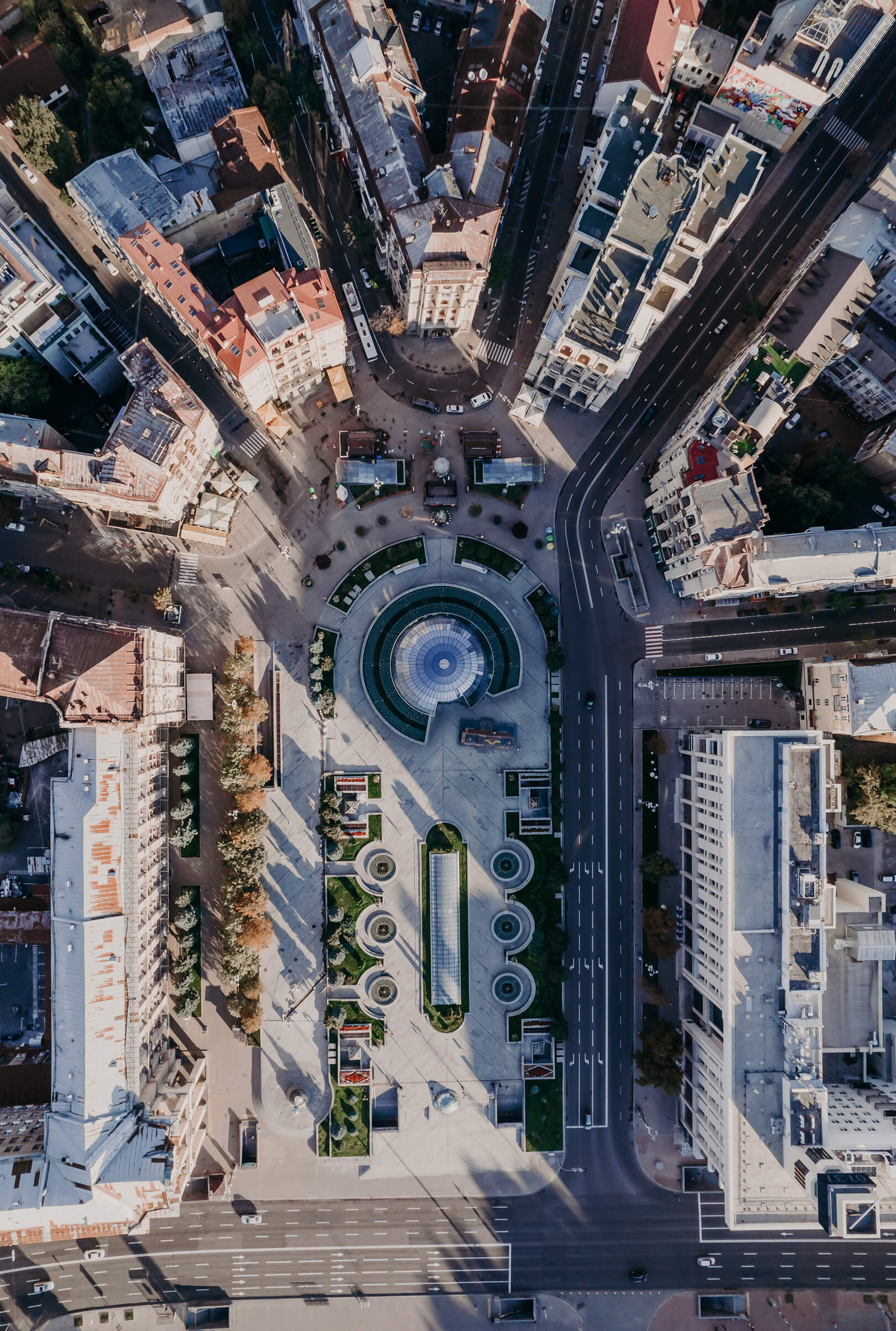 Aerial view of an urban square featuring a central circular fountain, surrounding greenery, and intersecting roads lined with buildings participating in an energy efficiency program.